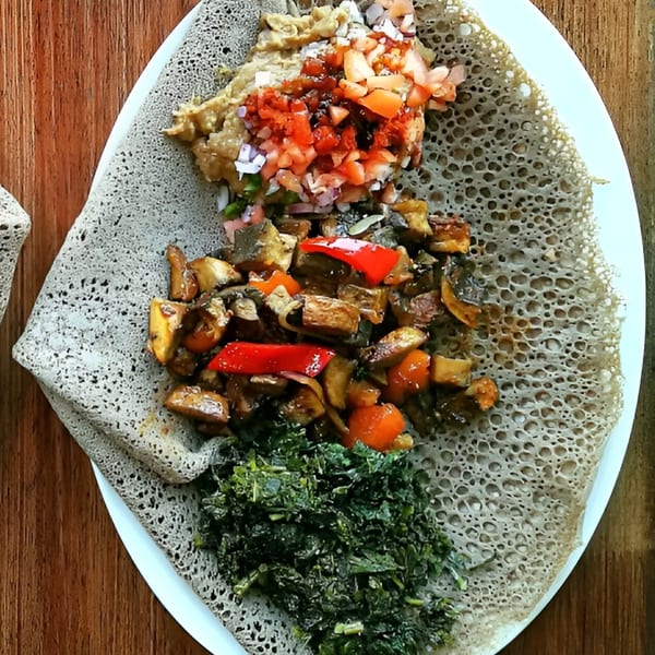 Ethiopian injera bread with three distinct toppings: a tomato mixture, sautéed vegetables, and greens.