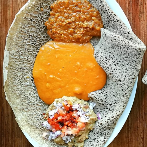 Ethiopian injera bread with three distinct servings of stews and chopped vegetables.